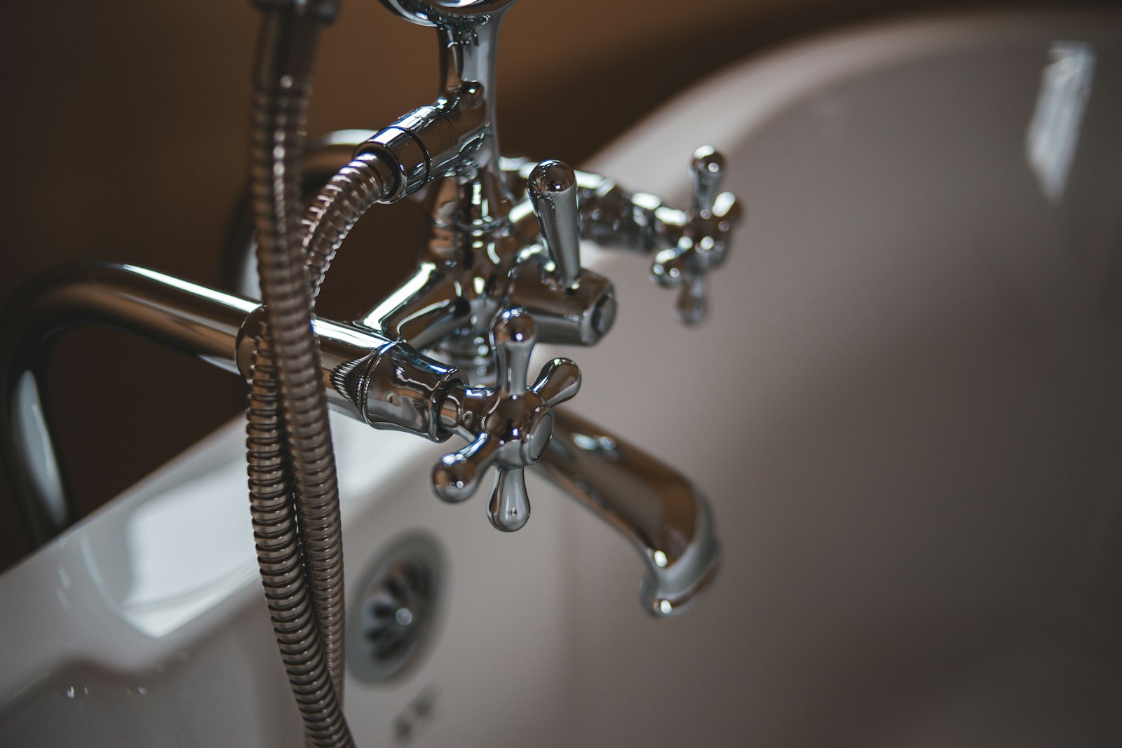 A polished chrome bath and shower mixer tap with hose over a white ceramic bath